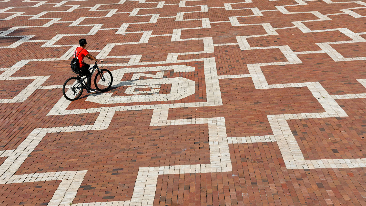 student rides a bike across the brickyard
