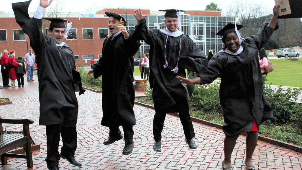 Students jump in the air wearing graduation gowns